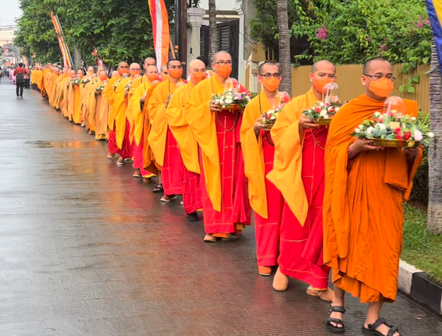 A group of men wearing orange robes and holding flowersDescription automatically generated with medium confidence